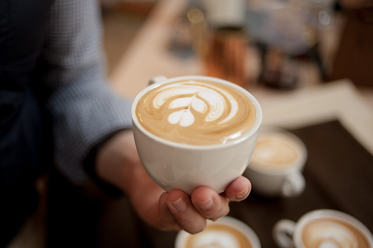 Latte art servido en una taza sostenida con las manos